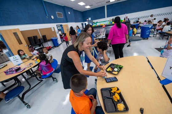 adult helping student in lunchroom open their milk