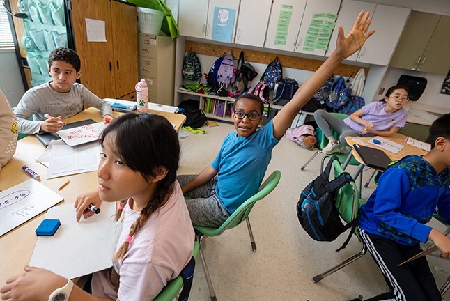 photo of students in a class with a male student raising his hand