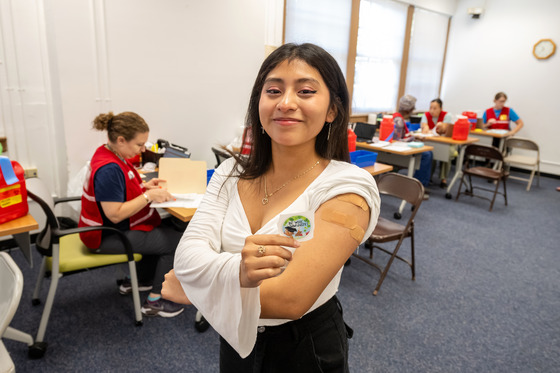photo of girl with bandaid after receiving her shot holding a sticker which reads 'Be Wise, Immunize'