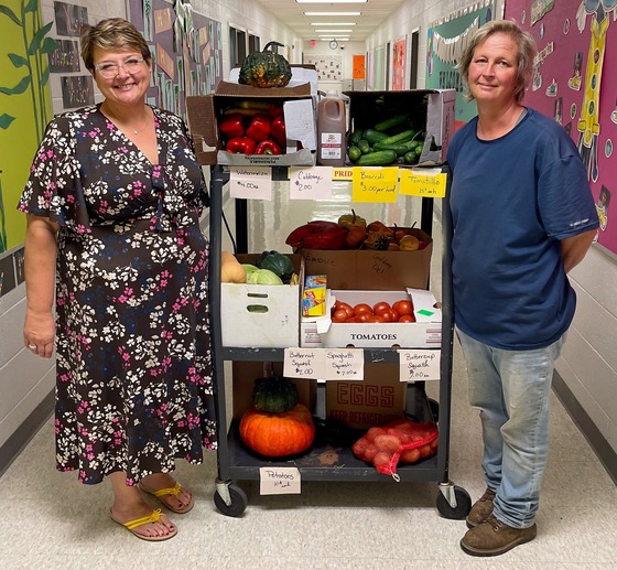 Two women standing on either side of cart with vegetables