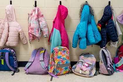 Children's coats hanging on hooks with backpacks on floor beneath