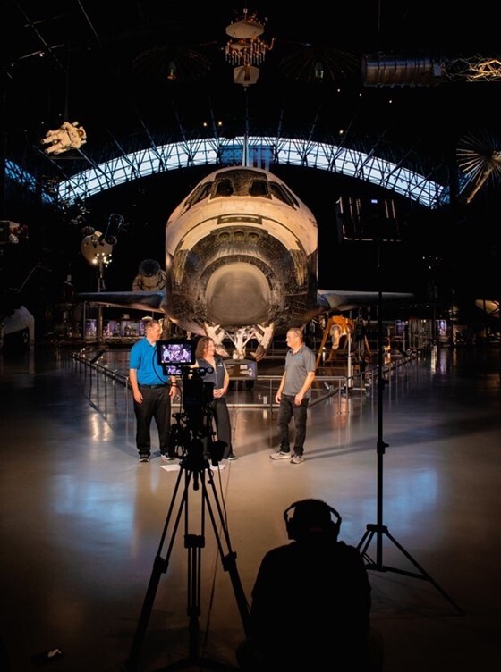 Mr. Kevin Smith being interviewed by reporters standing in front of space shuttle at Smithsonian National Air and Space Museum Udvar-Hazy Center
