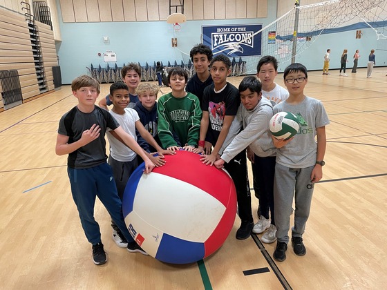 Group of students around a very large volleyball in the gymnasium
