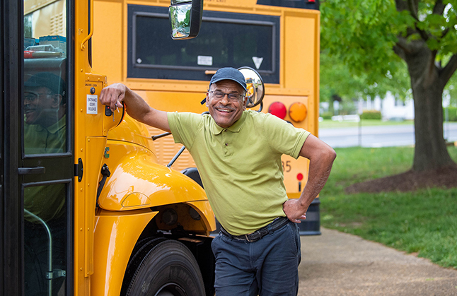 bus driver smiles and poses for a picture next to school bus