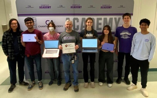 Teacher and students standing together holding laptop computers