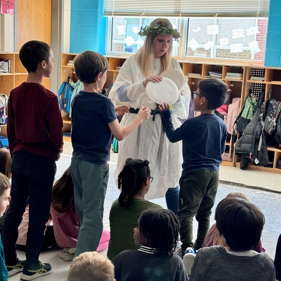 Third grade teacher Mrs. Murphy wears a robe and leaf crown while teaching about ancient Greece