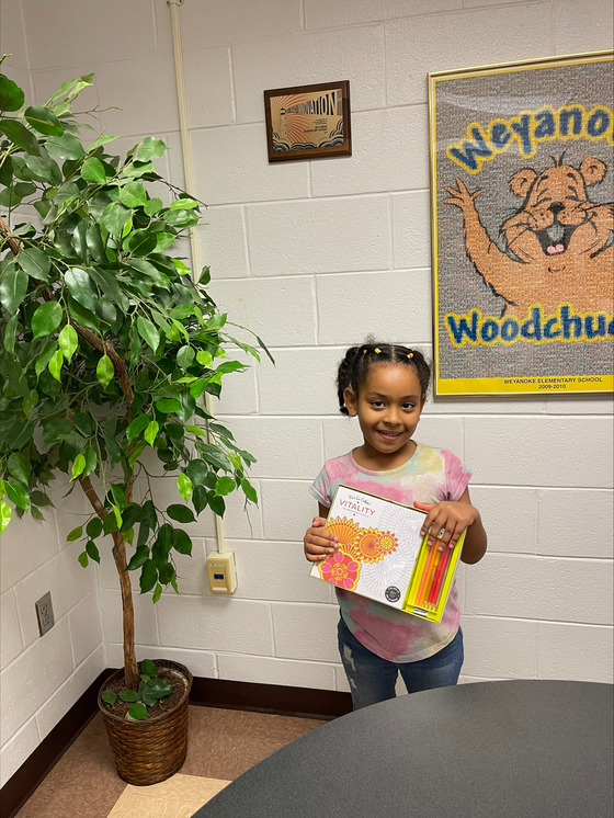 A studnet holding up a prize she won in the attendance raffle. It is a coloring book.