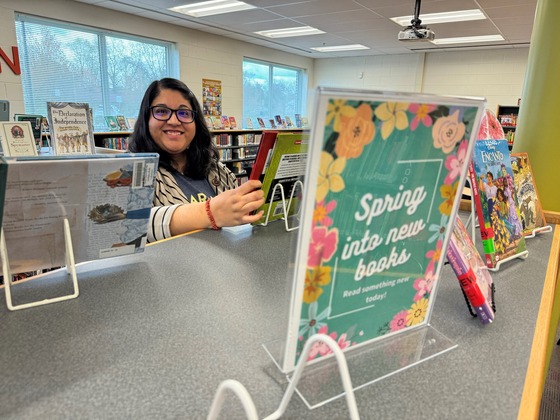 An image shows Clermont Librarian, Kannan Cangro, arranging books on display behind a sign that says "Spring into new books!"