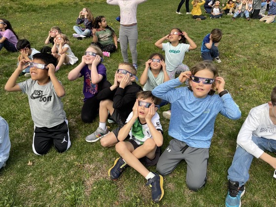 Students wearing eclipse safety glasses look to the sky.