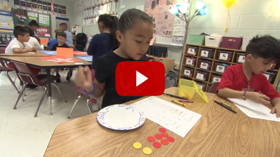 Students sitting at tables using buttons to count 
