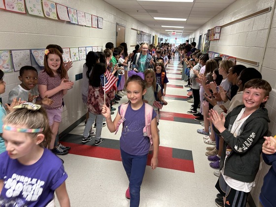 Military connected students, waving small American flags, walk through the halls as students and teachers applaud.