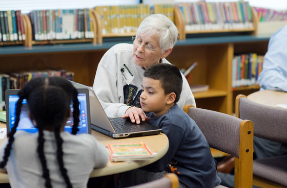 Senior volunteer working with a student at a laptop.