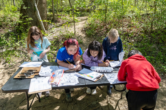 Elementary students around a table filled with papers, charts and graphs and engaged in outdoor data collection.