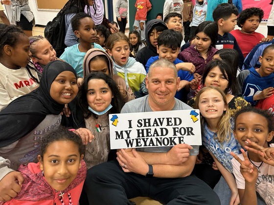 Mr. Shaffer holding a sign that says "I shaved my head for Weyanoke". He is surrounded by fourth grade students.