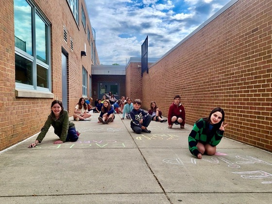 SCA members write chalk messages on the sidewalk outside the building. 