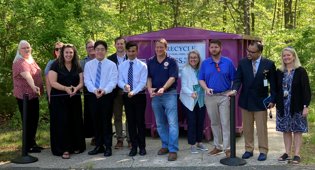 Students, staff, and community members cutting ribbon at purple glass recycling container