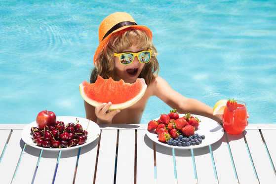 photo of boy by the pool in sunglasses eating watermelon
