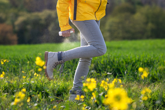 photo of person walking through a field spraying bug spray on leg