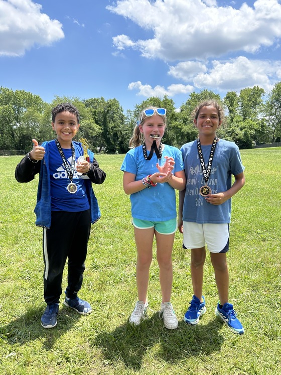 Students pose with Running at Recess trophies. One student bites their medal. 