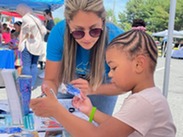 Summer Extravaganza event supporter guiding a young student through an activity.
