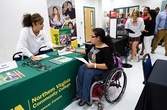 Woman at table giving handout to woman sitting in wheel chair