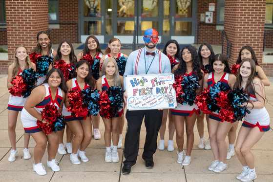 Counselor and  cheerleaders, holding a white board saying high five, and has his face painted blue and red. 