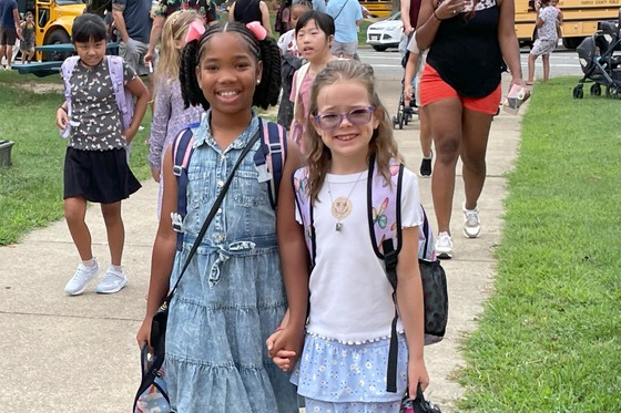 Two girls arriving at school near the school buses