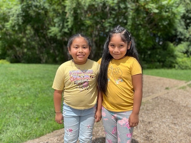 Two students link arms and smile while enjoying the beautiful weather outside. 