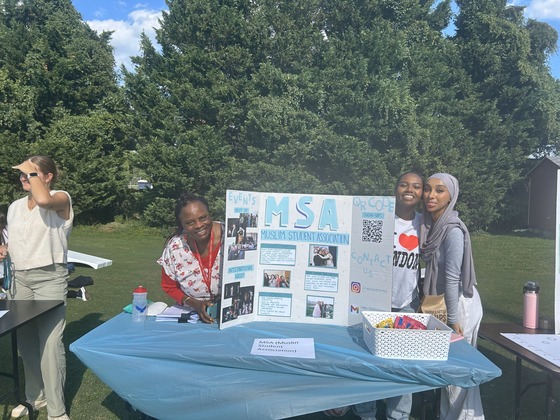 Students standing on either side of a poster, outside.