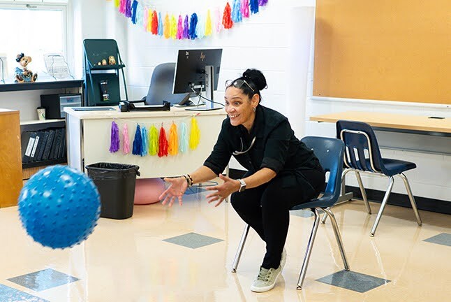 teacher throws a large bouncy ball while sitting down