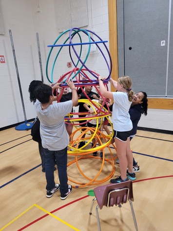 Students use hula hoops to build a spherical tower. 