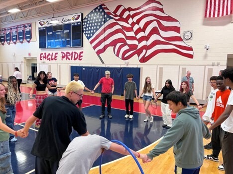 Students standing in a circle in the gym with a hula hoop