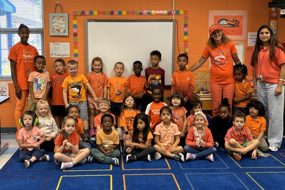 Kindergarten class wearing orange clothing standing in front of an orange wall