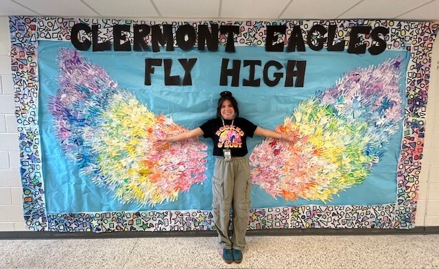 Madeline Deveney poses with Clermont students Wing artwork.