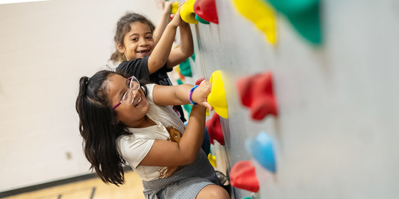 2nd grade students smile at the camera as they climb our famous rock wall 