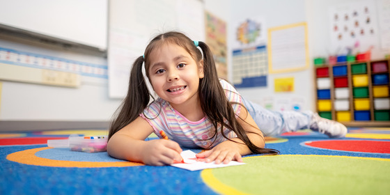 A kindergarten student lays on the carpet to write a story 