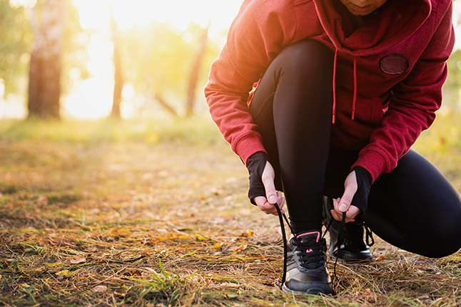 photo of someone tying shoe while out walking among fall leaves