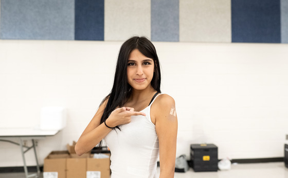 Photo of girl pointing to bandaid on her arm where she just received a vaccine