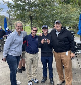 3 adults and 1 student holding a trophy outside