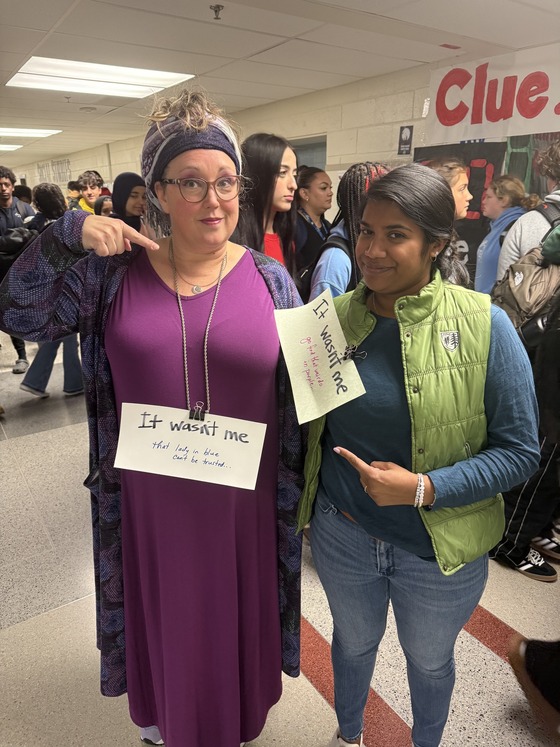 an adult and a student standing in the school hallway with other students in the back