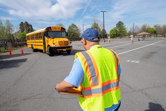 person with a safety vest watches a bus as the driver attempts to parallel park