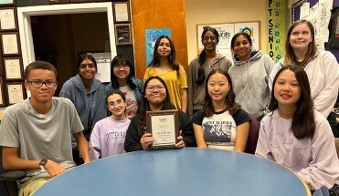 Students sitting and standing together holding award