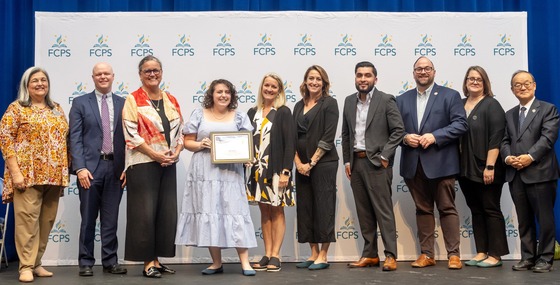 School Board Members, Dr. Reid, and staff standing together with teacher holding award