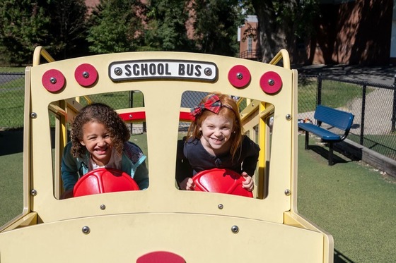 two students in a fake school bus on a playground smiling