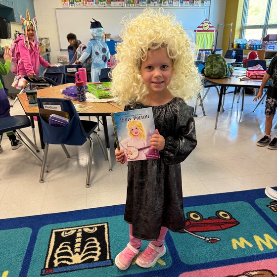 A student, dressed as Dolly Parton, holds up a Dolly Parton book.