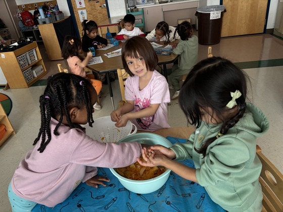 Three preschool students with their hands in pumpkin seeds and pulp