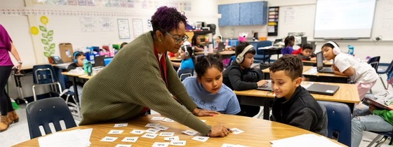 teacher leaning over a table and helping a student with an assignment