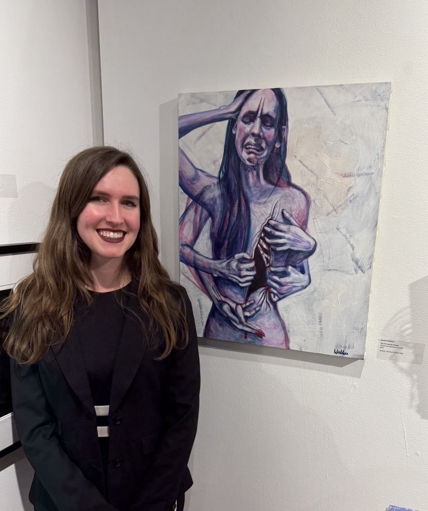 a teacher standing in front of her painting of a woman with a hand on her head and an upset face