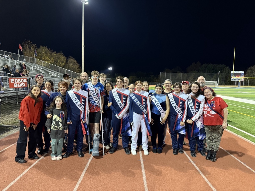 Marching band students standing on the track wearing senior sashes and their parents