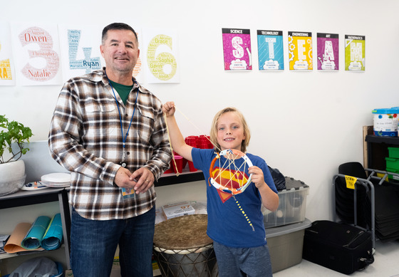 teacher smiling with student while student shows off dream catcher they made